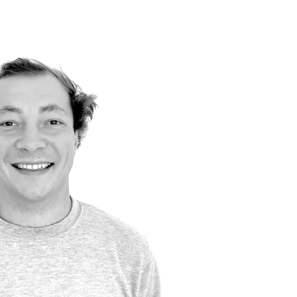 Une personne souriante aux cheveux courts portant une chemise à col roulé de couleur claire, représentée à partir des épaules sur le côté gauche d'un fond blanc, représente fiable livraison bagages sécurisée à travers l'Europe.