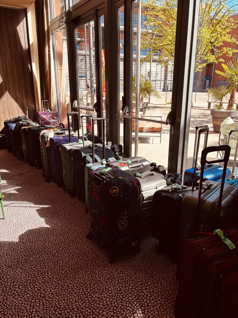 Une rangée de valises et de sacs de voyage aux poignées allongées, alignés contre des fenêtres allant du sol au plafond, la lumière du soleil entrant, et une cour avec des arbres visibles à l'extérieur - idéal pour livraison bagages sécurisée ou transport bagages Europe. Une rangée de valises et de sacs de voyage aux poignées allongées, alignés contre des fenêtres allant du sol au plafond, la lumière du soleil entrant, et une cour avec des arbres visibles à l'extérieur - idéal pour livraison bagages sécurisée ou transport bagages Europe.