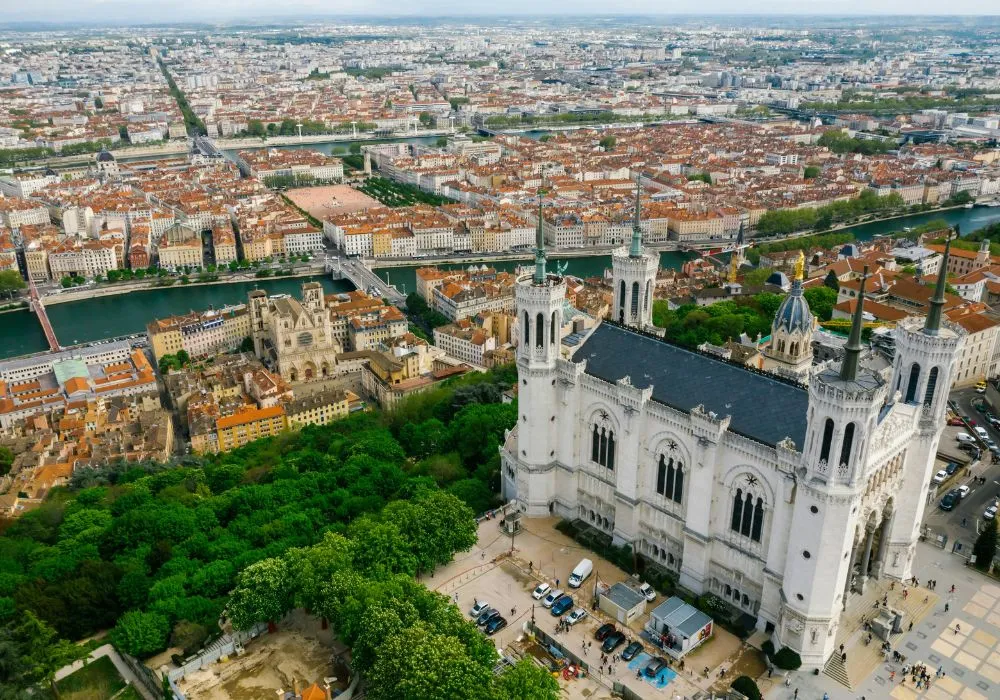 Vue aérienne de Lyon, France, avec la basilique Notre-Dame de Fourvière au premier plan, une végétation luxuriante et la Saône à l'arrière-plan. Découvrez les services pratiques de consigne bagages France à proximité pour des solutions sécurisées pour vos bagages.