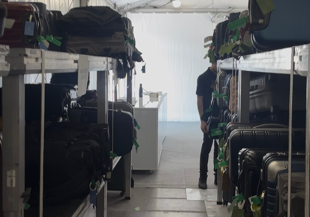 Des rangées d'étagères remplies de valises dans une pièce très éclairée ; une personne se tient à l'arrière-plan près d'un comptoir blanc, partiellement masqué par les étagères, présentant la consigne bagages France pour stockage bagages sécurisé.