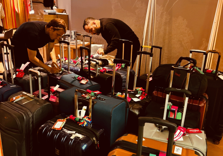 Deux personnes trient et étiquettent un grand groupe de valises pour le portage bagages événements à l'aide d'étiquettes rouges et vertes dans un environnement intérieur. Les bagages sont serrés et les deux personnes sont concentrées sur leur tâche.