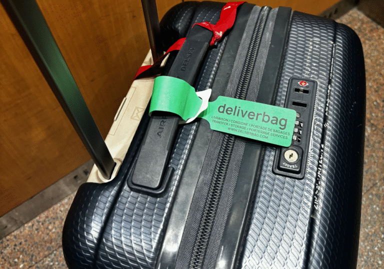 Une valise noire texturée avec une étiquette de bagage "deliverbag" et une sangle rouge, dotée d'une poignée allongée et de fermetures à glissière, est présentée sur un sol moucheté près d'un mur en bois - idéale pour les besoins de consigne bagages France ou de service bagagerie mobile. Une valise noire texturée avec une étiquette de bagage "deliverbag" et une sangle rouge, dotée d'une poignée allongée et de fermetures à glissière, est présentée sur un sol moucheté près d'un mur en bois - idéale pour les besoins de consigne bagages France ou de service bagagerie mobile.