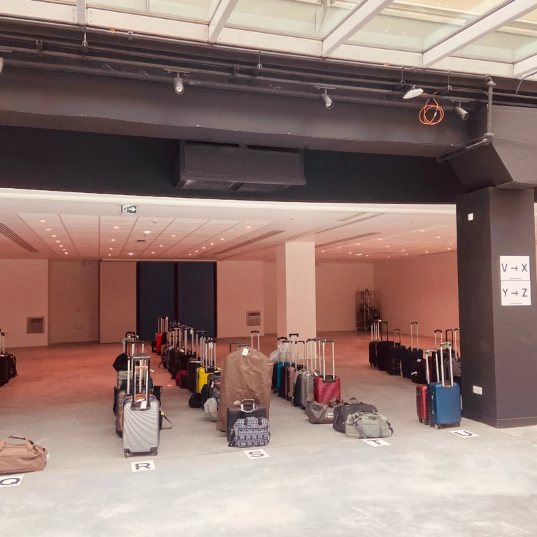 Un espace intérieur spacieux et lumineux avec des rangées de valises et de sacs alignés sur des lettres marquées au sol, mettant en valeur le portage bagages événements sous de hauts plafonds et un éclairage fluorescent.
