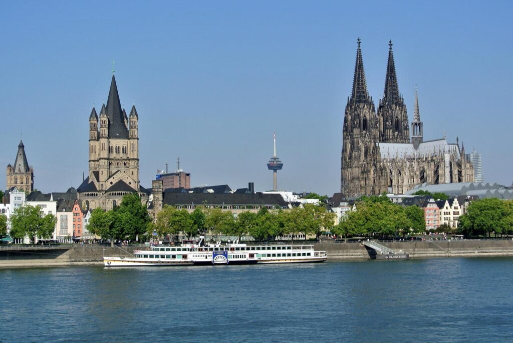 Vue pittoresque de Cologne, en Allemagne, avec les flèches jumelles de la cathédrale de Cologne, la grande église Saint-Martin, un bateau de croisière au bord du fleuve et des bâtiments modernes, le tout au bord du Rhin, sous un ciel bleu limpide.