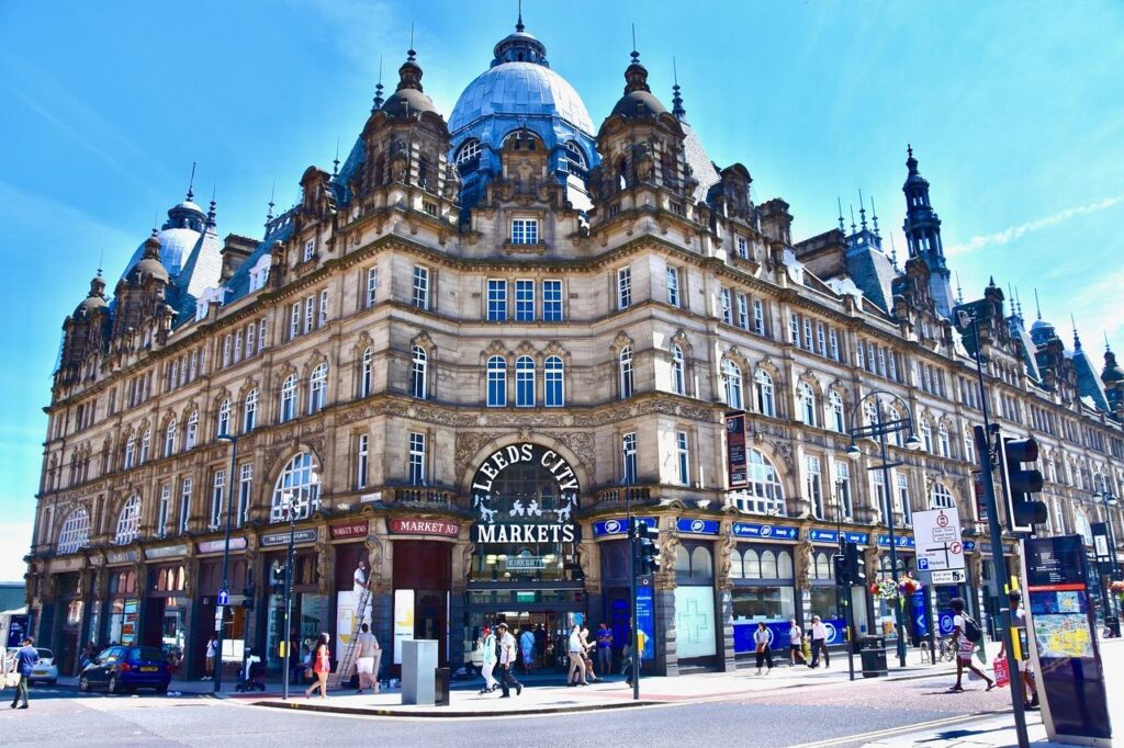 Un grand bâtiment historique orné d'un toit en dôme abrite les marchés de la ville de Leeds. Les gens marchent le long du trottoir et les boutiques s'alignent au rez-de-chaussée sous un ciel bleu éclatant. Un grand bâtiment historique orné d'un toit en dôme abrite les marchés de la ville de Leeds. Les gens marchent le long du trottoir et les boutiques s'alignent au rez-de-chaussée sous un ciel bleu éclatant.