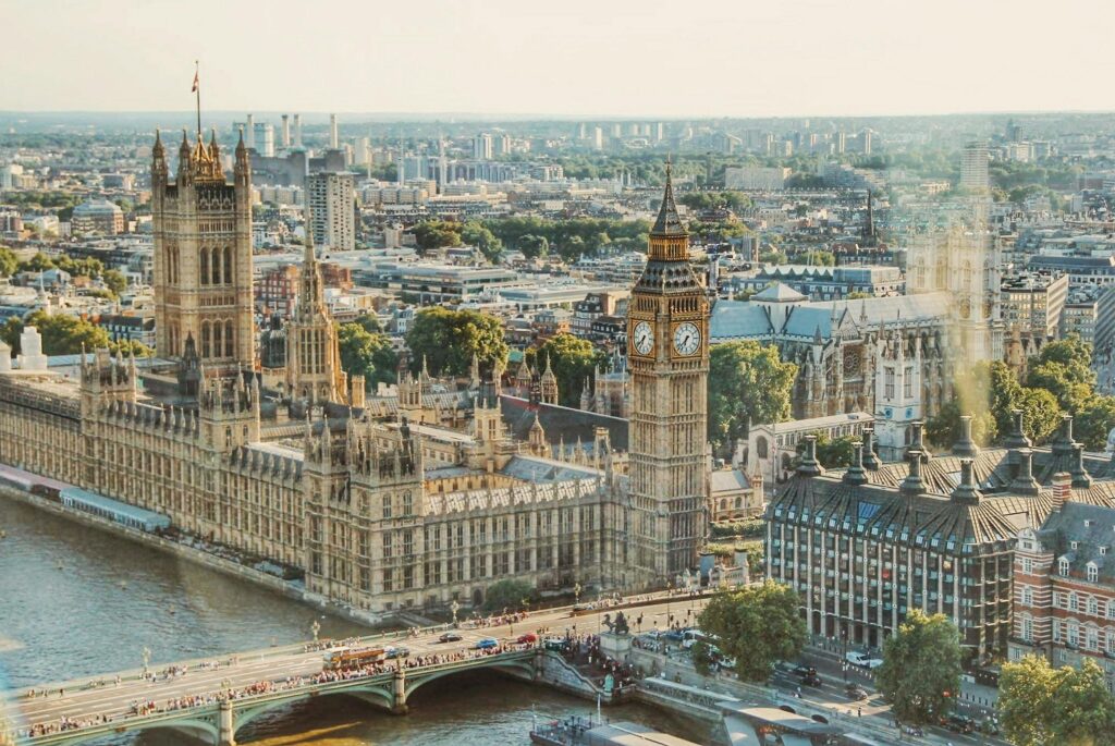 Vue aérienne du Palais de Westminster et de Big Ben au bord de la Tamise à Londres, avec le pont de Westminster et les bâtiments de la ville en arrière-plan par temps clair.