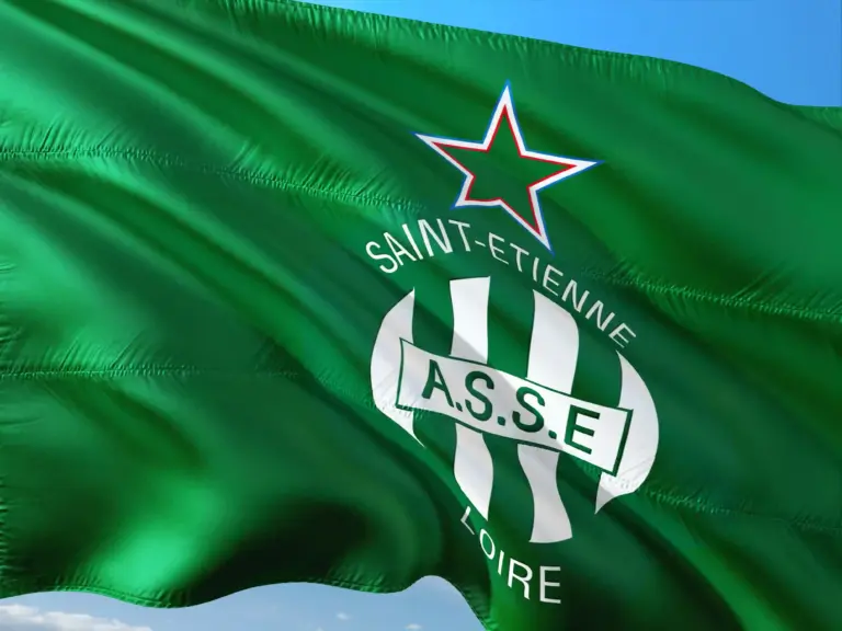 Drapeau vert à rayures blanches, orné d'une étoile au contour rouge et du texte « SAINT-ETIENNE LOIRE » inscrit en cercle autour du logo de l'A.S.S.E. Ce logo représente le club de football français AS Saint-Étienne. Ciel bleu en arrière-plan. Drapeau vert à rayures blanches, orné d'une étoile au contour rouge et du texte « SAINT-ETIENNE LOIRE » inscrit en cercle autour du logo de l'A.S.S.E. Ce logo représente le club de football français AS Saint-Étienne. Ciel bleu en arrière-plan.