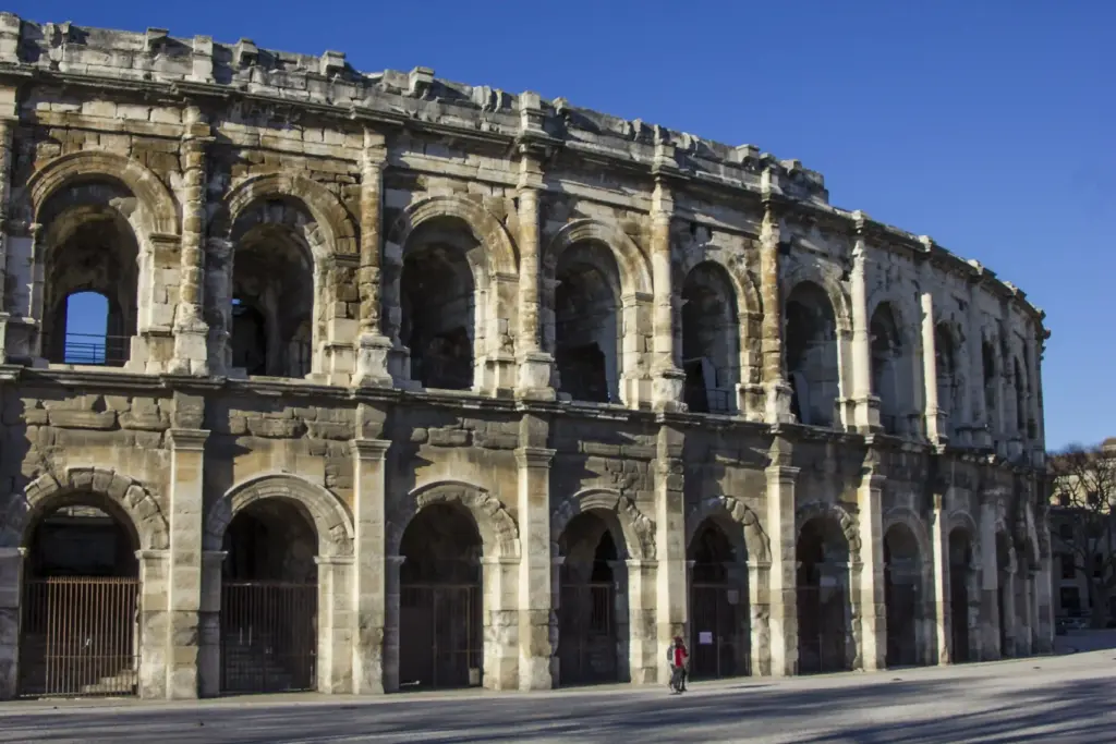 Un amphithéâtre romain antique aux multiples arcades sous un ciel bleu limpide ; une personne se tient près de la base, soulignant ainsi l'ampleur imposante de l'édifice. Un amphithéâtre romain antique aux multiples arcades sous un ciel bleu limpide ; une personne se tient près de la base, soulignant ainsi l'ampleur imposante de l'édifice.