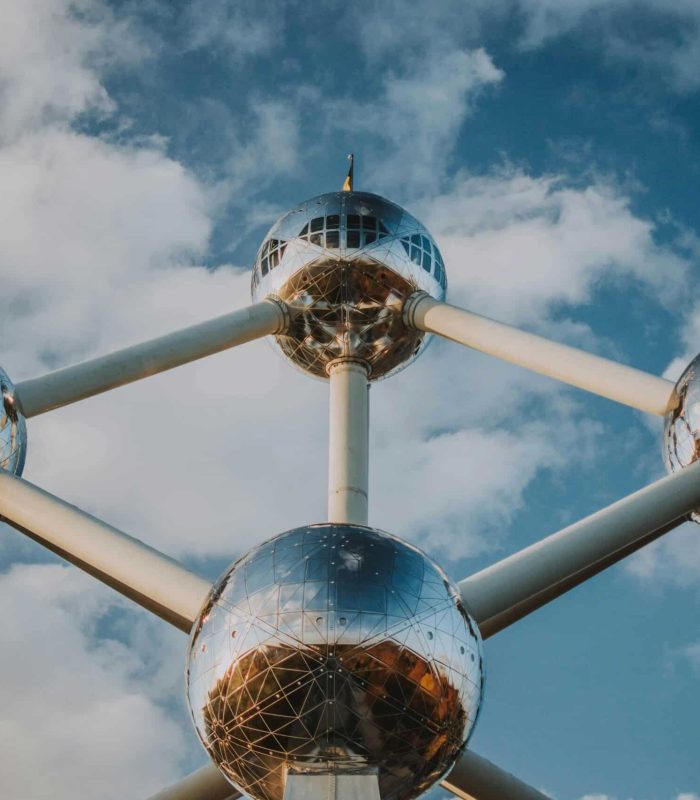 Vue rapprochée de l'Atomium, une structure futuriste composée de grandes sphères métalliques réfléchissantes reliées par des tubes, sur fond de ciel bleu partiellement nuageux.