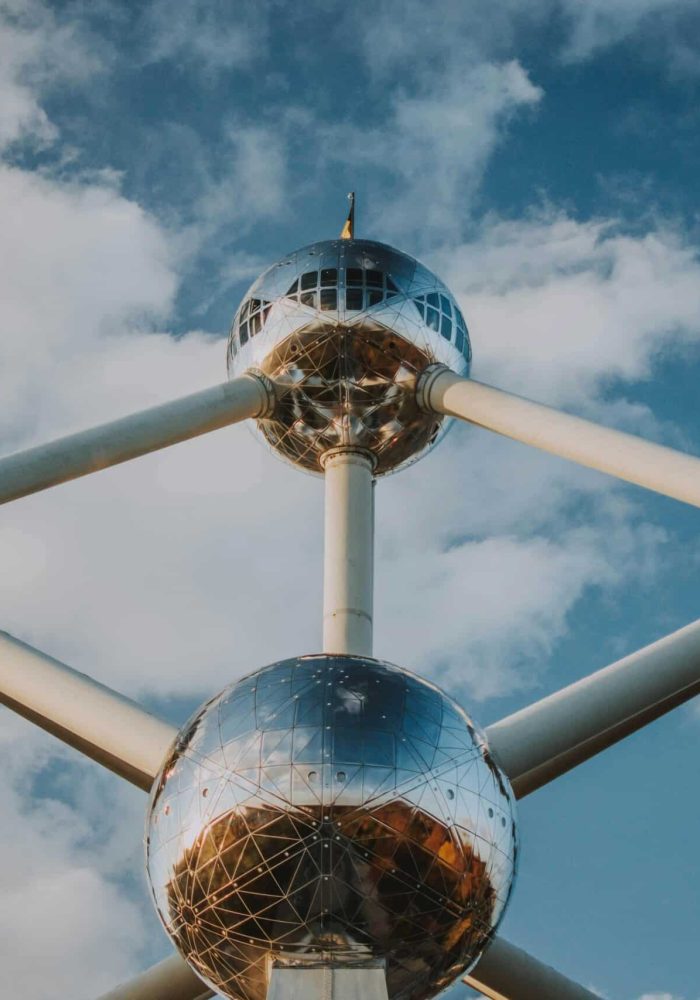 Vue rapprochée de l'Atomium, une structure futuriste composée de grandes sphères métalliques réfléchissantes reliées par des tubes, sur fond de ciel bleu partiellement nuageux.