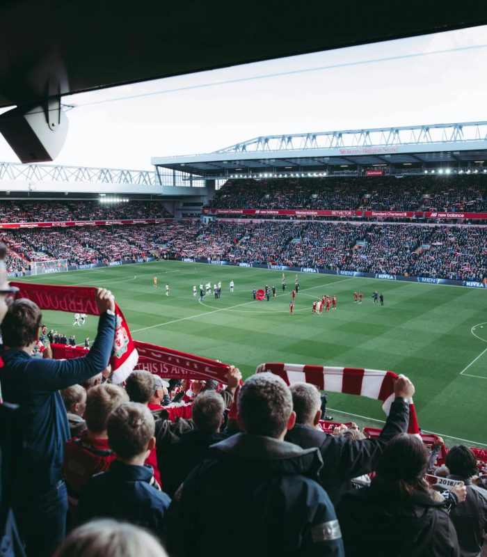 Une foule de supporters de football, dont beaucoup portent des écharpes rouges et blanches, applaudit dans un stade rempli de spectateurs alors que les joueurs se rassemblent sur le terrain avant un match.