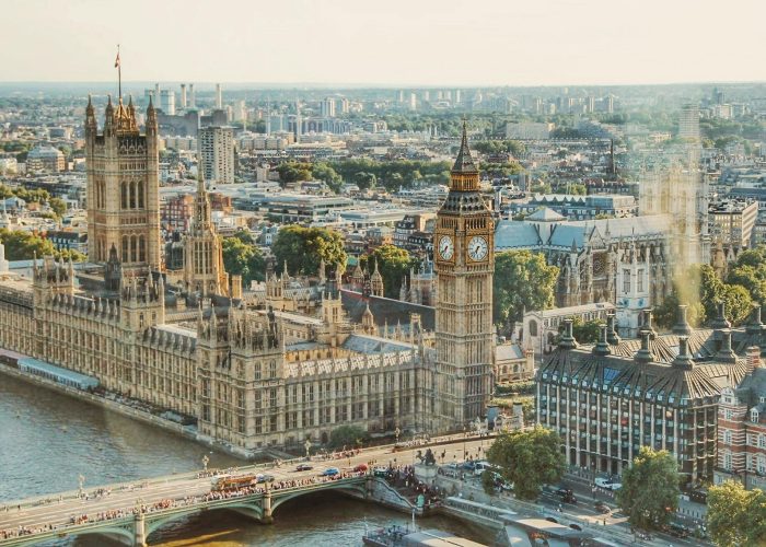 Vue aérienne du Palais de Westminster et de Big Ben au bord de la Tamise à Londres, avec le pont de Westminster et les bâtiments de la ville en arrière-plan par temps clair.