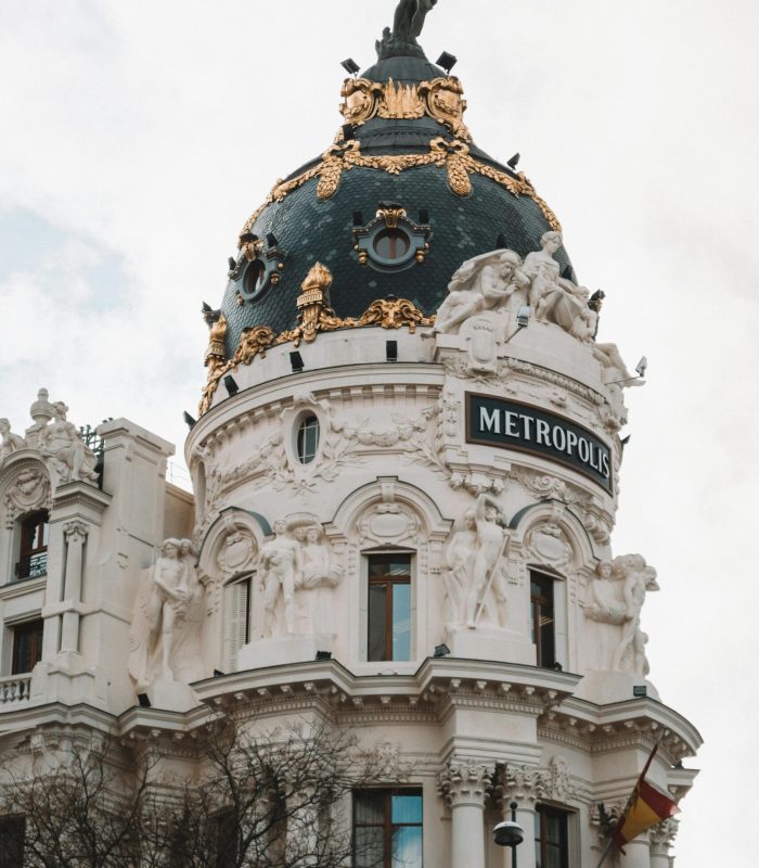 Le bâtiment Metropolis à Madrid, en Espagne, est doté d'un grand dôme décoré de touches d'or, de statues et d'une sculpture d'ange au sommet. Le drapeau espagnol est visible en bas à droite.