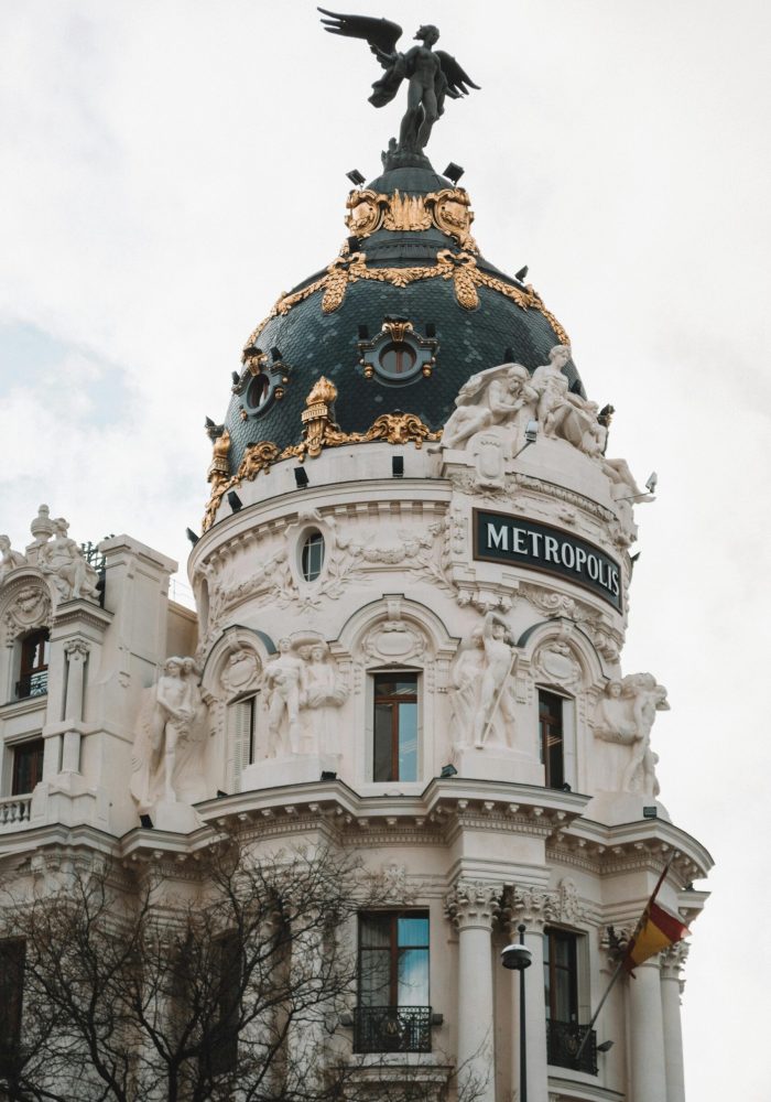 Le bâtiment Metropolis à Madrid, en Espagne, est doté d'un grand dôme décoré de touches d'or, de statues et d'une sculpture d'ange au sommet. Le drapeau espagnol est visible en bas à droite.