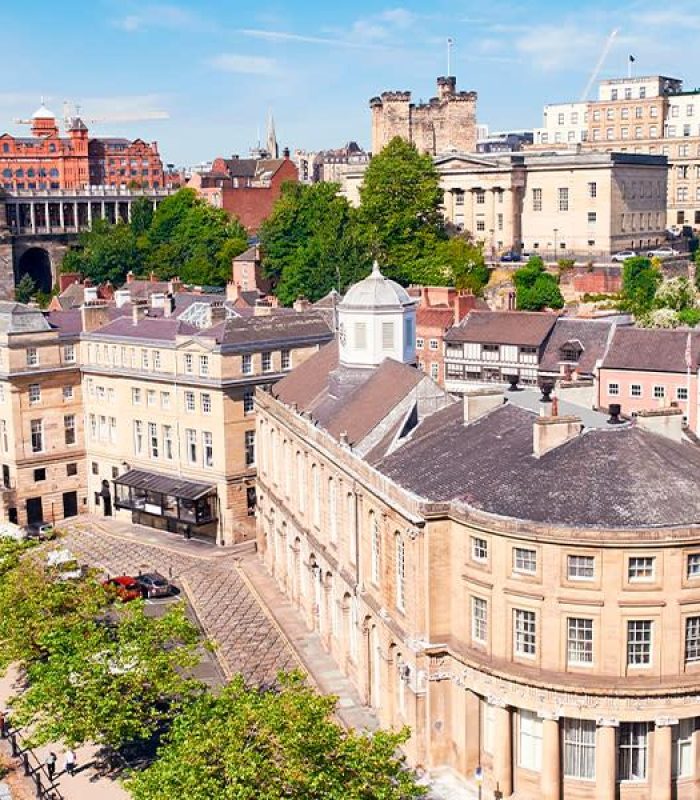 Vue aérienne de Newcastle upon Tyne, avec des bâtiments historiques, des ponts en arc et la rivière Tyne, par une journée ensoleillée avec un ciel bleu clair.