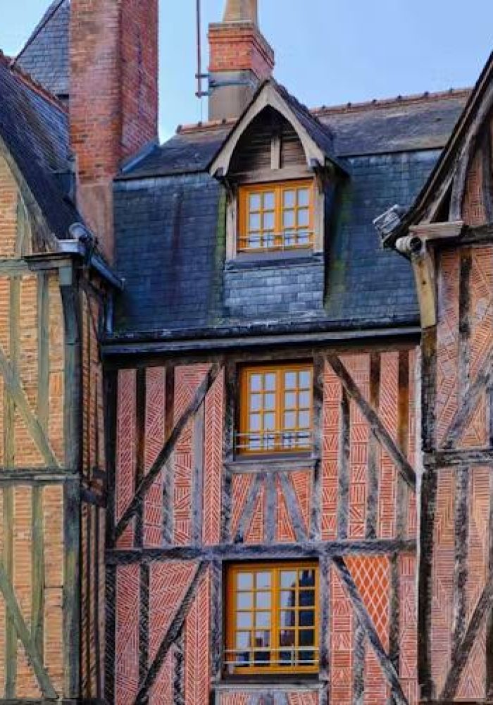 Vue rapprochée de trois maisons historiques à colombages avec des poutres en bois apparentes, des briques et des toits d'ardoise abrupts, mettant en valeur l'architecture médiévale sous un ciel dégagé.