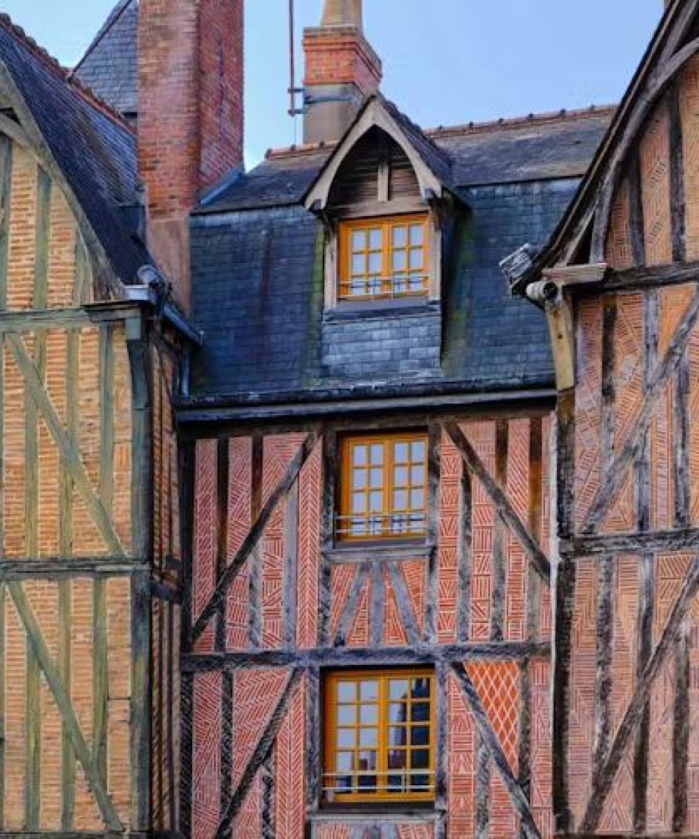 Vue rapprochée de trois maisons historiques à colombages avec des poutres en bois apparentes, des briques et des toits d'ardoise abrupts, mettant en valeur l'architecture médiévale sous un ciel dégagé.
