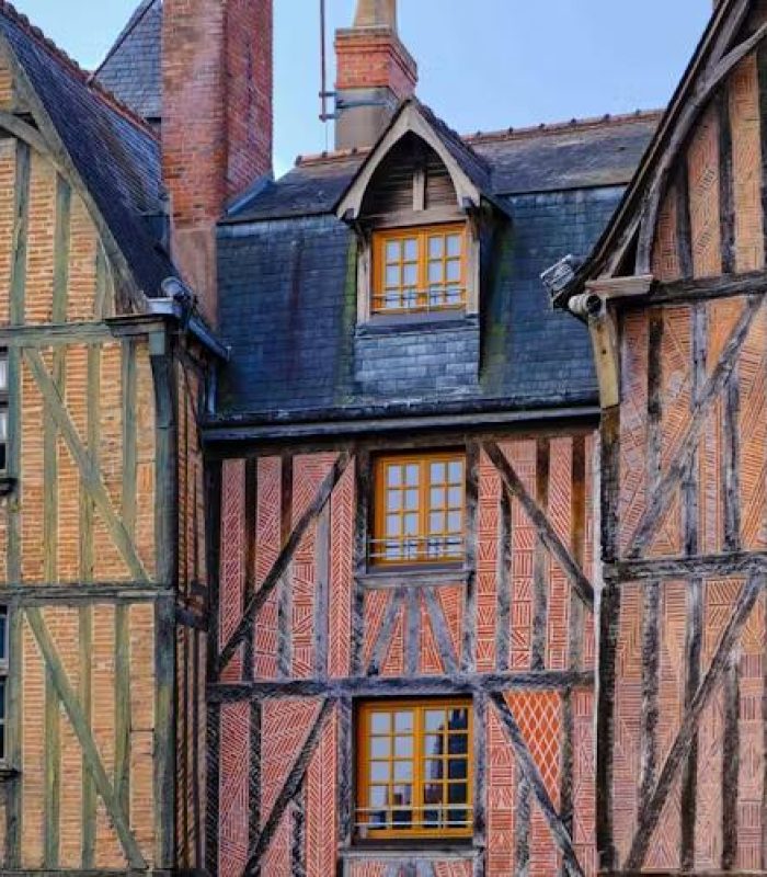 Vue rapprochée de trois maisons historiques à colombages avec des poutres en bois apparentes, des briques et des toits d'ardoise abrupts, mettant en valeur l'architecture médiévale sous un ciel dégagé.