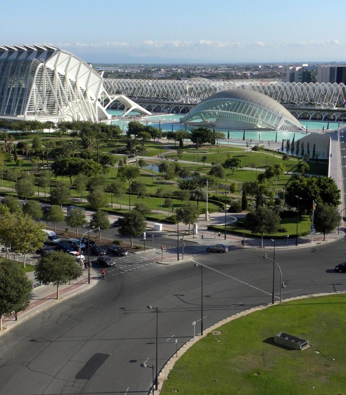 Vue large de la Cité des arts et des sciences de Valence, en Espagne, avec ses bâtiments modernes à l'architecture blanche, ses parcs verdoyants et ses routes sinueuses, sous un ciel bleu clair.