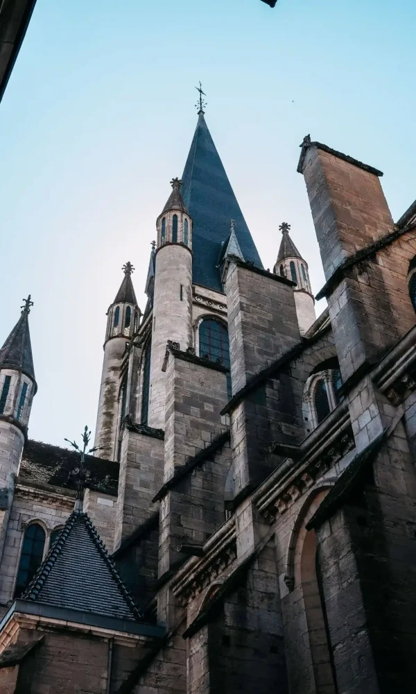 Église en pierre de style gothique, avec ses hautes flèches pointues et ses fenêtres cintrées, photographiée en contre-plongée sur fond de ciel bleu limpide.